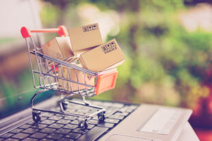 Cardboard parcels in a miniature shopping trolley, on a laptop